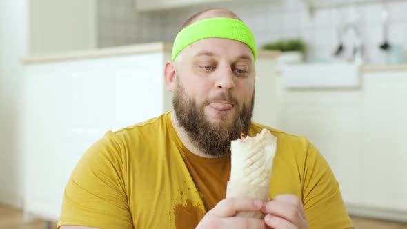 Portrait of Sweaty Fat Man in Yellow Wet Sportswear Is Eating Danar in Kitchen