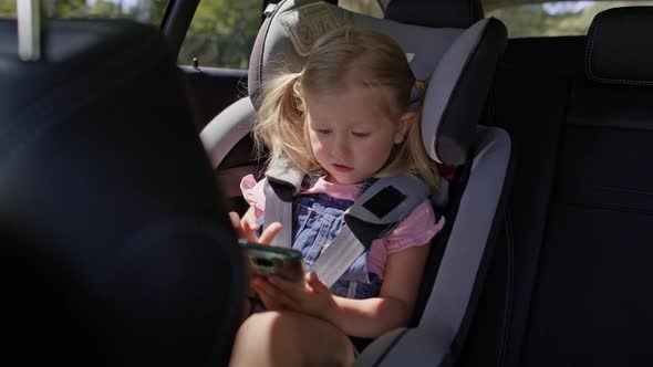 Video of little girl on rear seat of car with phone. Shot with RED helium camera in 8K. alt
