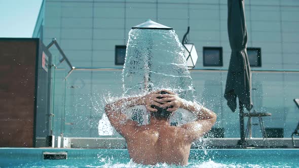Tourist on vacation at the hotel stands under the summer shower in the pool with blue water alt