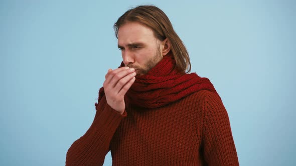 Male Has a Sore Throat and Coughing Looking Ill While Posing Against Blue Studio Background alt
