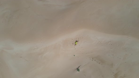 Aerial View of Woman Laying on Sand Dune with Drone Flying Towards Her