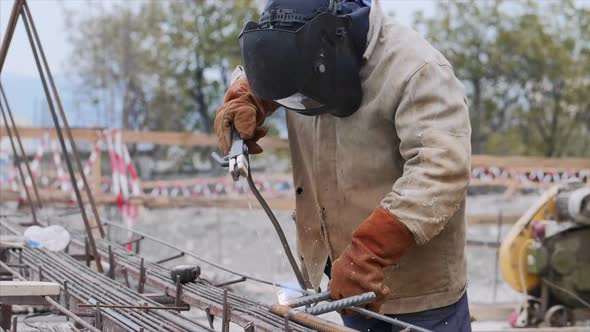Welder at Construction Site is Welding Pipe with Electrode in Helmet