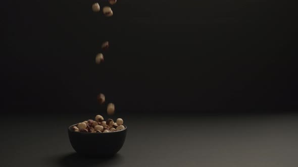 Slow Motion Roasted Hazelnuts Fall Into Black Bowl on Black Paper Background alt