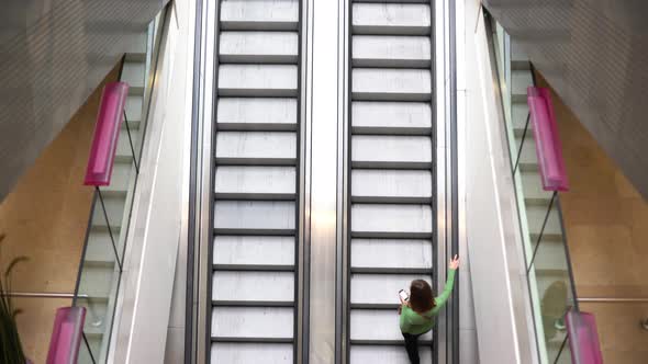 Woman looking at smartphone while riding up escalator