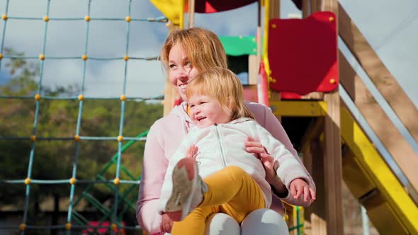 A smiling young mother and her little child are playing on the playground. alt