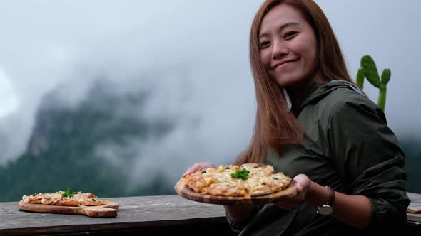 A young asian woman showing a plate of pizza in the outdoor restaurant