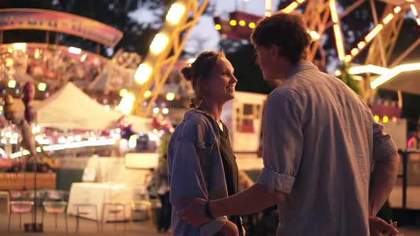 Side Portrait of an Attractive Young Couple Meeting in an Amusement Park with a Colorful Brightful alt