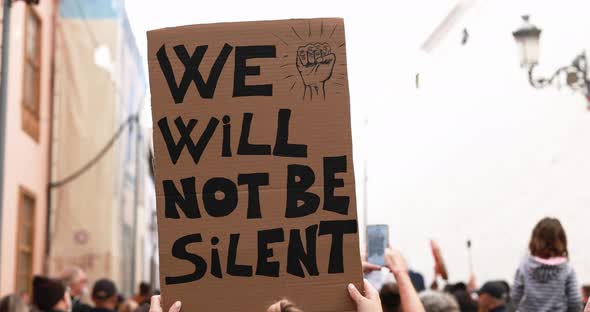 Young woman walking with crowd on a demonstration holding banner alt