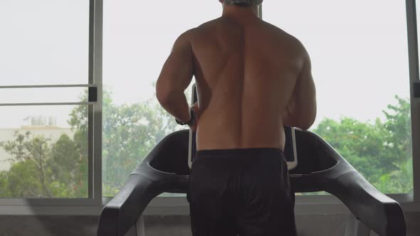Muscular topless man running on treadmill in fitness