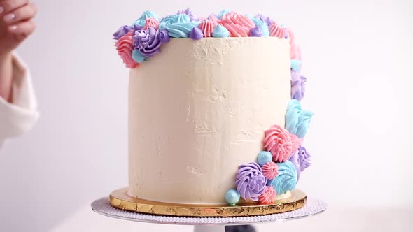 Baker piping pastel color buttercream rosettes on a white cake to make a unicorn cake. alt