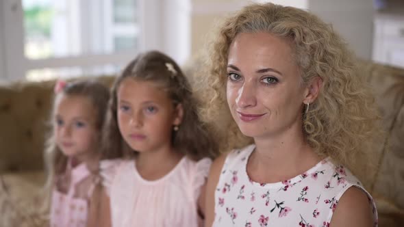 Attractive Caucasian Woman Sitting with Blurred Girls at Home Looking at Camera Smiling alt