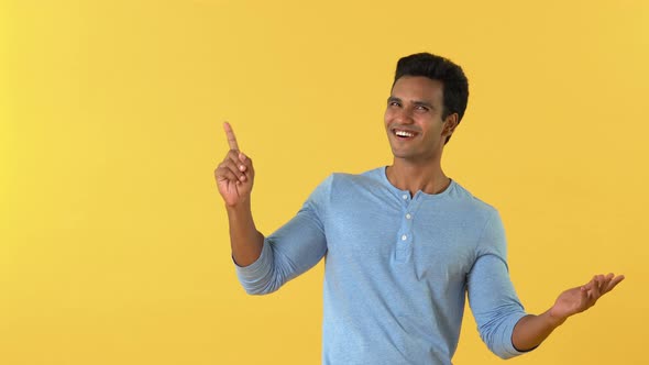 Smiling young Indian man opening hand and pointing to copy space