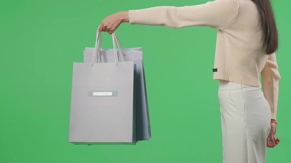 Side View Of A Shopping Woman Holding Shopping Bags Up While Standing In Front Of Green Screen alt