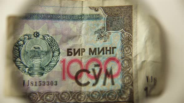 One thousand Uzbekistan Sum and a magnifying glass. alt