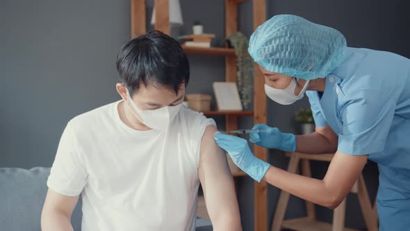 Young Asia lady nurse giving Covid-19 or flu antivirus vaccine shot to male patient.