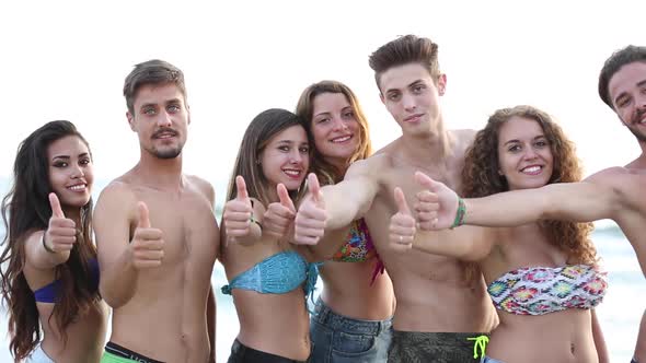 Multicultural group of friends at beach showing thumbs up