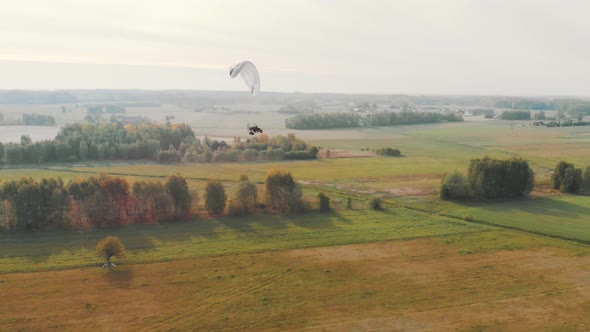 Aerial View of a Paramotor Gliding Through the Air Over Green Fields alt