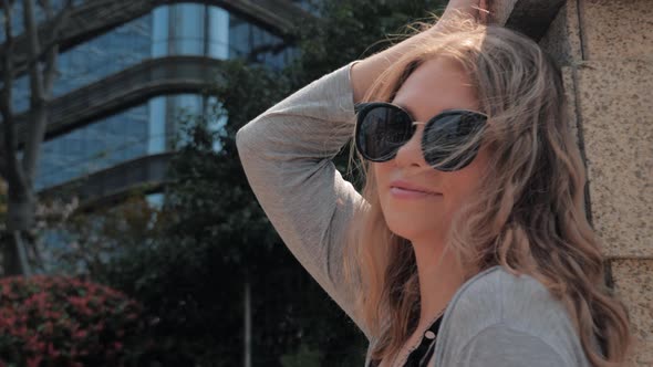 Portrait of Beautiful Girl in Sunglasses is Relaxing Leaning on a Wall in City Street in Sunny Day alt