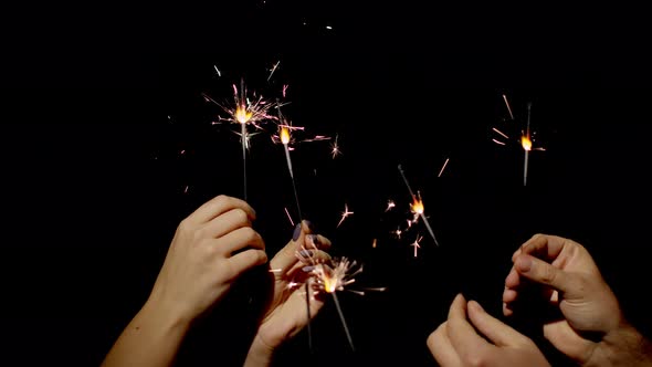 Hands Holding and Waving Bengal Fires. New Year Sparkler Candle Burning on a Black Background alt