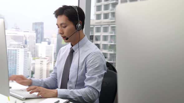 Handsome Asian man wearing microphone headset working in call center office as a telemarketer