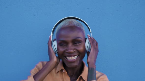 Happy senior Afro woman having fun dancing and listening music with wireless headphones alt