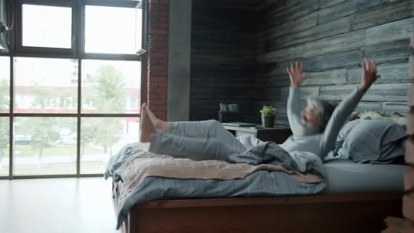 Slow Motion of Mature Man Wearing Pajamas Jumping in Bed at Home Enjoying Rest Alone alt
