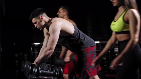 Men and Woman Taking Dumbbells From the Stand in the Gym alt