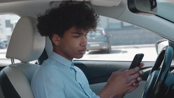Portrait of Black Man Browsing Smartphone is Sitting a Car Sunny Day in Parking alt