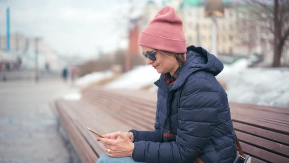 A Young Woman in a Hat and Sunglasses Using Her Smartphone and Drinking Coffee alt
