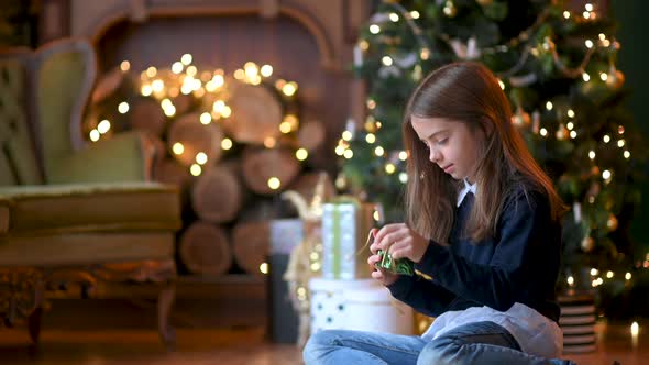 cute little girl sitting on the floor near the Christmas tree opens gifts