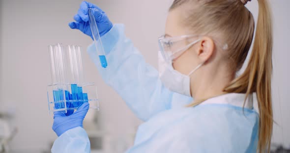 Female Scientist Holding Tubes and Flask with Liquid in Hands. alt