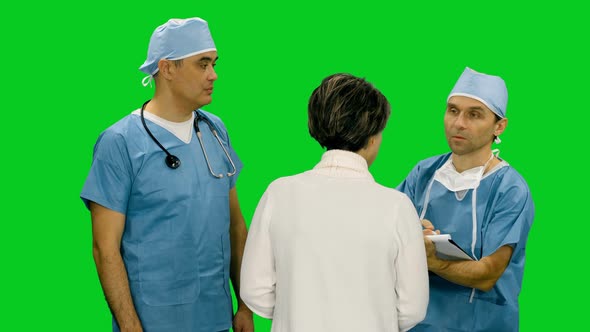 Two Doctors Talking To Female Patient And One Medic Writing On Clipboard