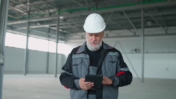 Portrait of Adult Grayhaired Man in a Protective Helmet Technical Engineer Stands and Uses a Screen alt