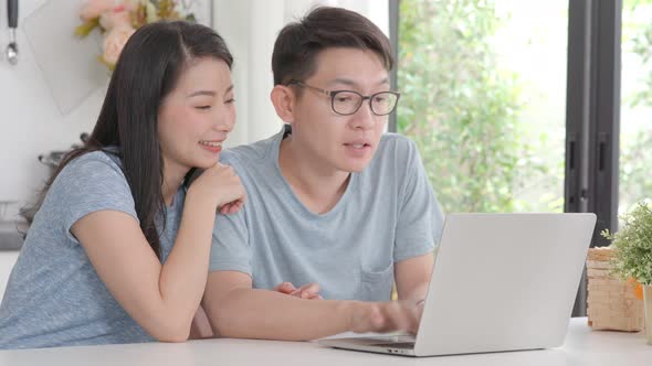Young Asian couple using laptop computer for shopping searching online at home