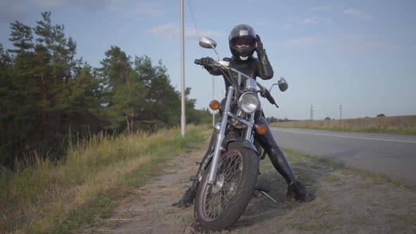Front View of the Successful Confident Young Woman in Leather Dress Sitting on Her Bike at the Road alt