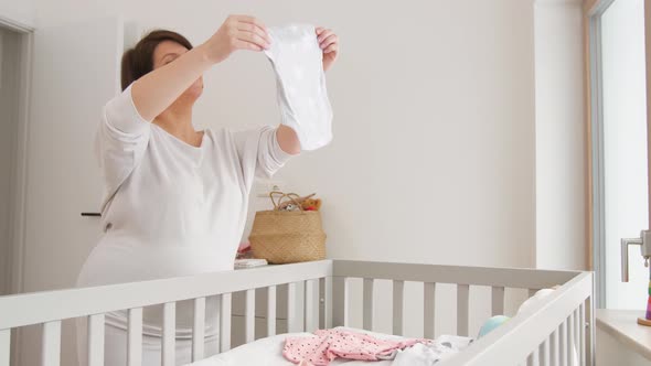 Happy Pregnant Woman Setting Baby Clothes at Home 8 alt