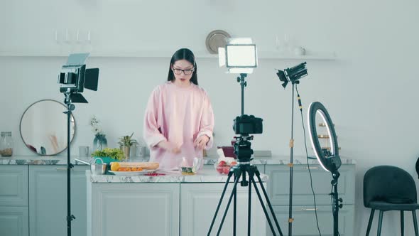 Young Cheerful Woman is Cutting Food While Filming in a Vlog alt