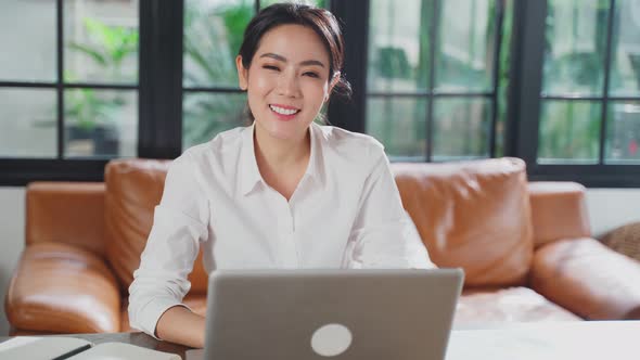 Portrait of Asian businesswoman working on computer at home and looking at camera with smile. alt