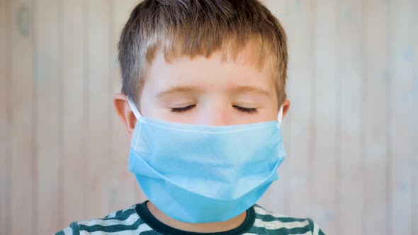 Little Boy in a Medical Facemask Looking at the Camera Blinking and Smiling. Small Boy's with Brown alt