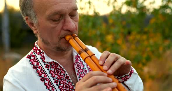 Large Portrait of a Male Musician in a Folk Ukrainian Costume Playing on a Wooden Pipe Pinching the alt