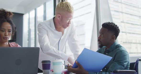 Diverse business people discussing with disabled colleague and documents in creative office alt