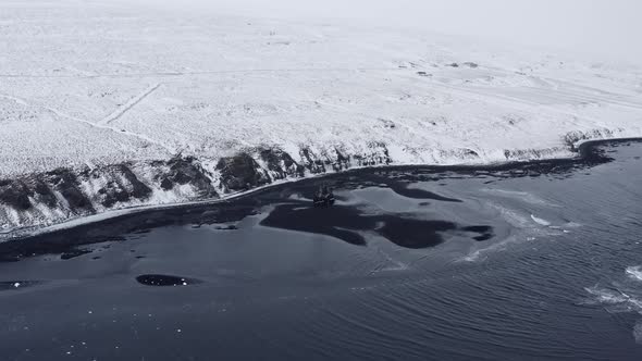 Drone Over Low Tide On Black Sand Beach Towards Snowy Landscape alt