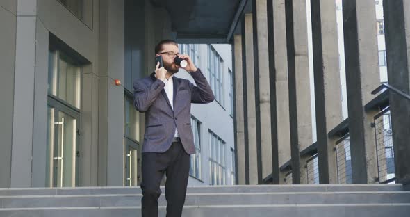 Office Worker in Glasses and Stylish Suit which Drinking Coffee and Talking on Phone alt