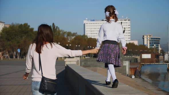 School Girl is Walking on Railing of Seafront with Mom Steadicam Rear View