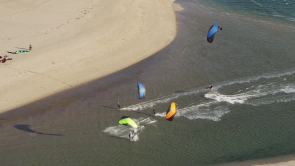 Aerial droene shot of a group of kite surfers racing up a river on a beach doing tricks and flips on alt
