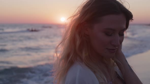 Young Blonde Woman with Wavy Hair Standing on Beach By the Sea on Sunset