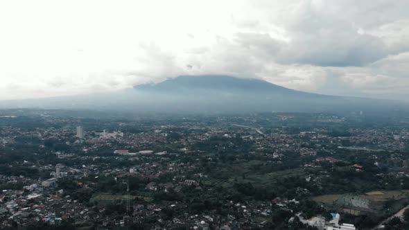 Cinematic aerial view of a mountain with white clouds surrounds it in a rural area.