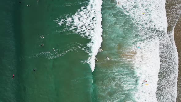 Surfers from above in Praia da Arrifana in west Portugal Atlantic coast, Aerial top view lowering ro alt
