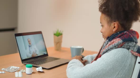 Young African Female in Selfisolation Communicates with a Doctor By Video Call Using a Laptop a alt