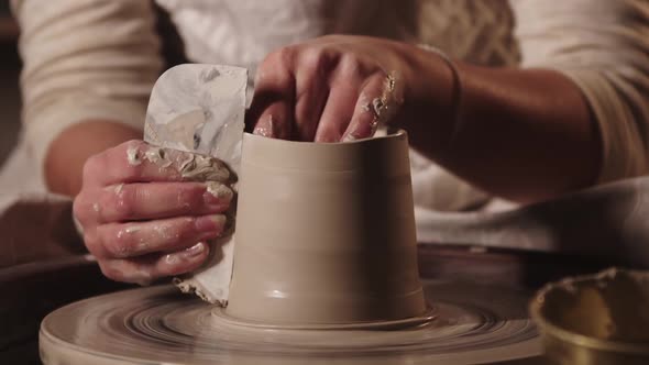 Pottery Workshop  Young Woman Potter Smoothening the Sides on the Pot Using a Tool alt